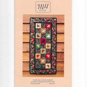 Könnte beinhalten: Ein Papiergrundmuster für einen gesteppten Tischläufer. Der Läufer hat ein Patchwork-Design mit roten, grünen und beigen Quadraten, jedes mit einem Blattmotiv. Der Rand ist ein Blumenmuster. Der Text lautet "Tumbling Leaves Runner".