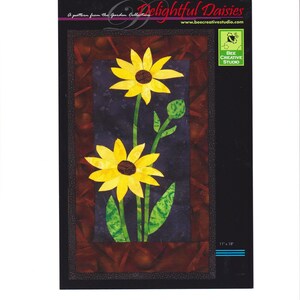 May include: A fabric panel featuring a floral design of yellow daisies with brown centers and green leaves. The artwork is set against a dark blue and brown background, with the text "Delightful Daisies" and "A pattern from the Garden Collection". The panel measures 11" x 18".