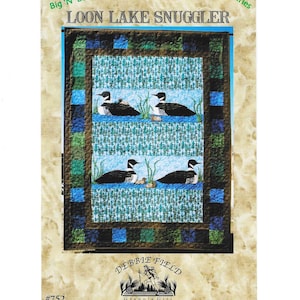 May include: A quilt with a central panel featuring four loons on a lake, with the text "LOON LAKE SNUGGLER". The quilt has a blue, green, and brown border. The text "Northwoods Big 'N' Easy" and "in A Series" are also visible.