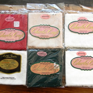 May include: Six packaged bread covers in various colors, including red, beige, white, and dark green. Each package features a label with the text "Bread Cover" and "Charles Craft" or "M&G Textiles". The covers are 14 count and measure 18 x 18 inches.