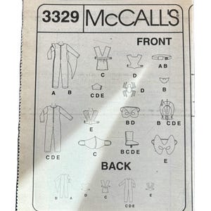 May include: A sewing pattern for a costume with the number 3329 and the brand name McCall's. The pattern includes instructions for making a jumpsuit, a cape, a mask, and a belt. The pattern is labeled "Front" and "Back" and includes different pieces labeled with letters.