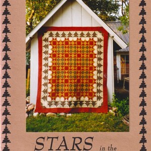May include: A quilt pattern booklet titled Prairie Designs Stars in the Forest PRD108. The cover features a photograph of a red, orange, and brown star-patterned quilt with a tree border, framed by a border of small black pine tree icons.