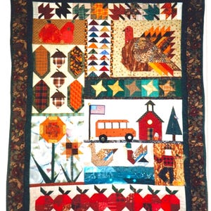 Könnte beinhalten: Ein rechteckiger Wandbehang-Quilt mit dunklem Blumenrand und einer hölzernen Aufhängestange. Das Mittelteil zeigt herbstliche Patchwork-Motive, darunter Kürbisse, Eicheln, einen Truthahn, einen Schulbus, ein Schulhaus, Enten und Äpfel.