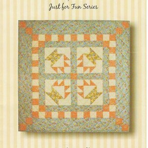 May include: A quilt pattern titled "Cake Walk" with dimensions of 26 x 26 inches. The quilt features a central design of four squares with star-like patterns in yellow and orange, surrounded by a border of orange and white squares and a floral patterned edge.