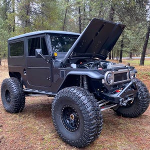 Può includere: Un veicolo fuoristrada nero con sospensioni rialzate e pneumatici grandi. Il cofano è aperto, mostrando il motore.