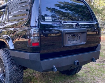 May include: Black 4Runner SUV with a black rear bumper, a tow hitch, and a US flag decal on the back window. The vehicle has a black license plate and a "4Runner" emblem.