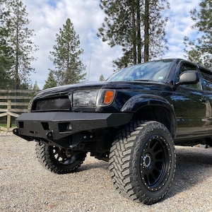 Pode incluir: Toyota 4Runner preta com um para-choques preto de reposição e rodas pretas. O veículo está estacionado em uma entrada de cascalho com árvores no fundo.