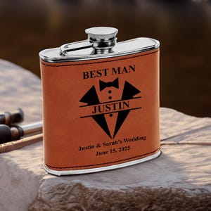 May include: A brown leather-wrapped stainless steel flask with the text "Best Man" and a tuxedo graphic. The flask is personalized with the name "Justin" and the text "Justin & Sarah's Wedding June 15, 2025".