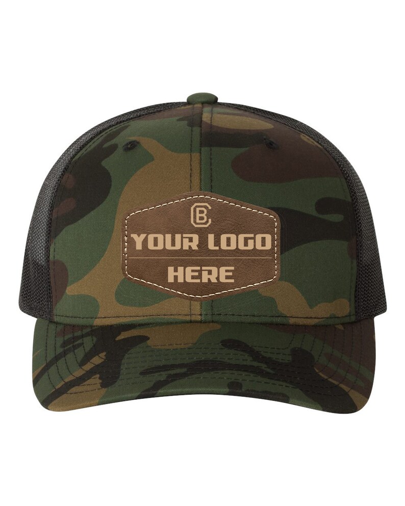May include: A camouflage trucker hat with a brown leather patch that says "YOUR LOGO HERE" in a tan font.