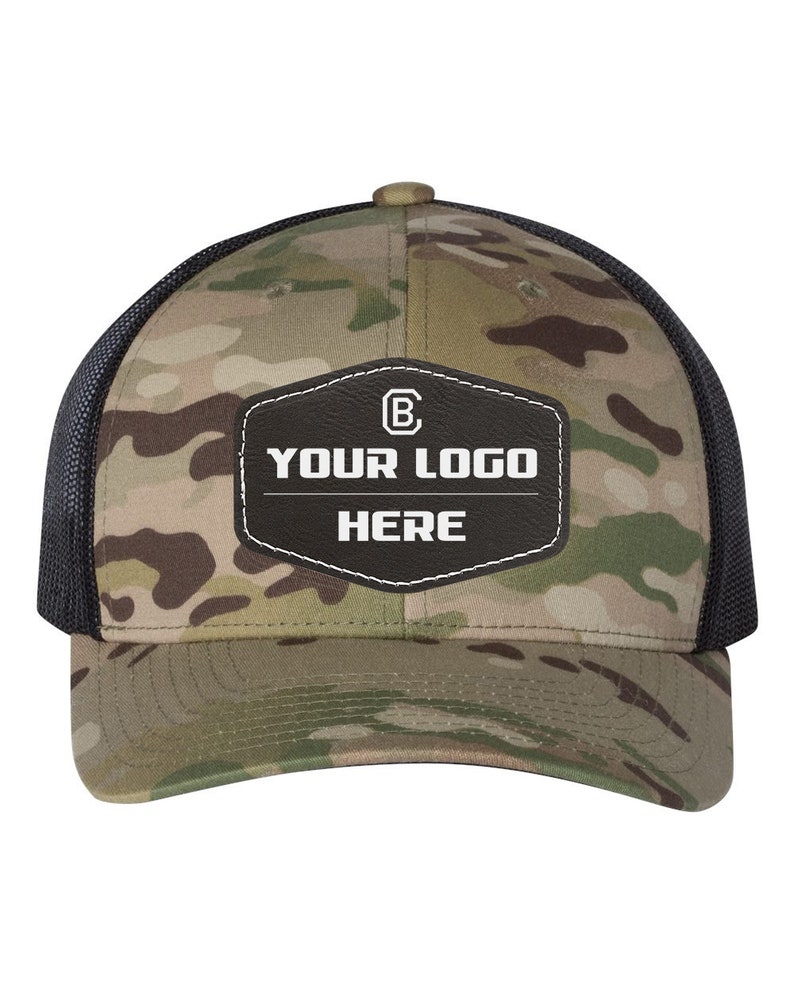 May include: A camouflage trucker hat with a black mesh back. The hat has a black leather patch with white stitching and the text "YOUR LOGO HERE" and a letter "B" inside a circle.