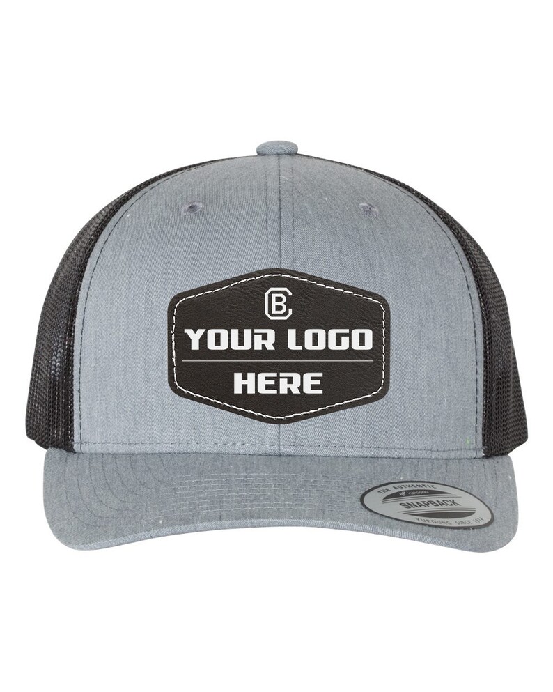 May include: A gray and black trucker hat with a black leather patch that says "YOUR LOGO HERE" and a white letter "B" inside a circle.