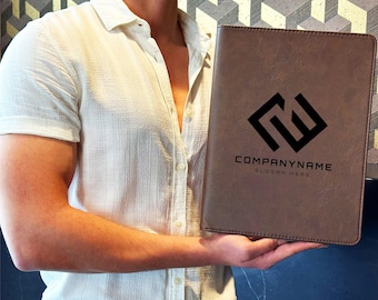 May include: A brown rectangular portfolio folder with a textured surface. The front features a black geometric logo above the text COMPANYNAME and SLOGAN HERE. The folder is held upright, showcasing its smooth, professional design and clean edges.
