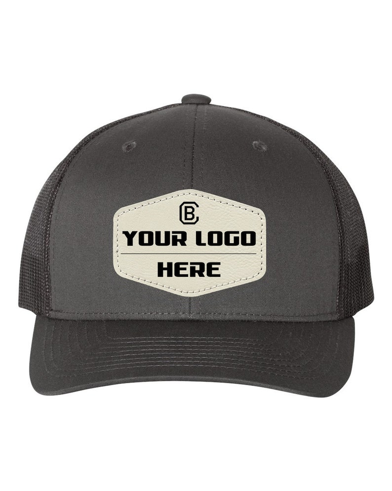 May include: A gray and black trucker hat with a white patch that says "YOUR LOGO HERE" and a black "B" inside a circle.