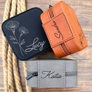 Pu&ograve; includere: Tre piccole scatole per gioielli personalizzate. Le scatole sono in similpelle e hanno una chiusura a zip. Le scatole sono in nero, marrone e grigio. Le scatole sono incise con i nomi "Lucy", "Sandra" e "Katia".