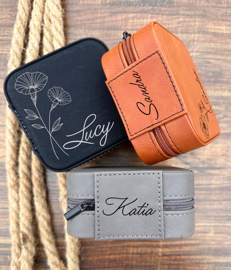 Pu&ograve; includere: Tre piccole scatole per gioielli personalizzate. Le scatole sono in similpelle e hanno una chiusura a zip. Le scatole sono in nero, marrone e grigio. Le scatole sono incise con i nomi "Lucy", "Sandra" e "Katia".