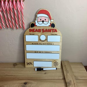 Könnte beinhalten: Holzschild mit einer Illustration von Weihnachtsmann und den Worten "Lieber Weihnachtsmann". Das Schild hat leere Felder, in die ein Kind sein Alter, seine Lieblingssache an Weihnachten und seinen grössten Weihnachtswunsch schreiben kann. Das Schild ist mit einer Schneeflocke verziert.