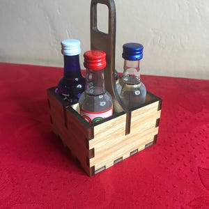 K&ouml;nnte beinhalten: Holz-Flaschenhalter mit Griff, der drei Miniaturflaschen mit blauen, roten und wei&szlig;en Kappen h&auml;lt.