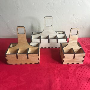 K&ouml;nnte beinhalten: Zwei Holz-Flaschentr&auml;ger mit Griffen. Der gr&ouml;&szlig;ere Tr&auml;ger hat sechs F&auml;cher und der kleinere vier. Beide Tr&auml;ger sind aus hellbraunem Holz mit schwarzen Kanten.