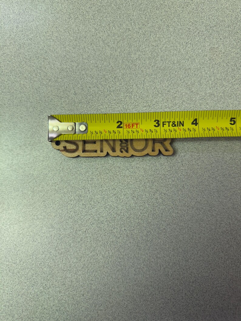 Może przedstawiać: Drewniany znak z napisem "Senior" i rokiem "2023". Znak jest mierzony ż&oacute;łtą miarą.