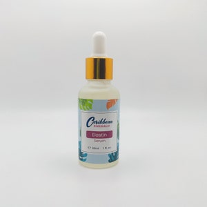 Puede incluir: Una botella de vidrio transparente con una tapa dorada y un gotero. La botella está etiquetada "Caribbean Emerald Elastin Serum" y contiene 30 ml o 1 fl. oz. de producto.