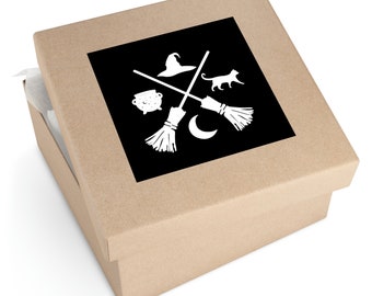 May include: A brown cardboard box with a black square sticker. The sticker features a white silhouette of a witch's hat, two broomsticks crossed, a cauldron, a cat, and a crescent moon.