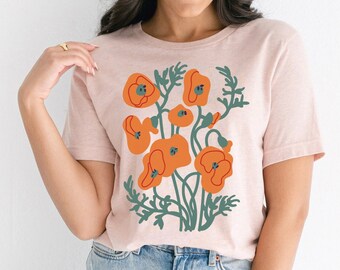 May include: A pink t-shirt with a floral print of orange poppies and green leaves.