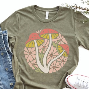 May include: A green t-shirt with a circular design of stylized mushrooms and flowers in shades of pink, yellow, and red.