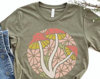 Puede incluir: Una camiseta verde con un diseño circular de setas y flores estilizadas en tonos rosa, amarillo y rojo.