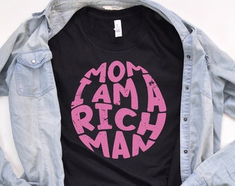 May include: Black t-shirt with a pink circle graphic that says "I am a rich man" in a distressed font.