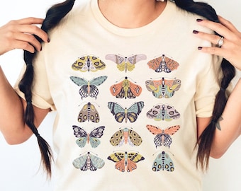 May include: A cream-colored t-shirt with a pattern of colorful butterflies. The butterflies are in various shades of pink, blue, green, yellow, and orange.