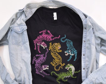 May include: A black t-shirt with a colorful graphic of five tigers in a circle. The tigers are in various poses and colors, including pink, blue, green, and yellow.