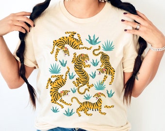 May include: A cream colored t-shirt with a graphic print of five orange and black tigers with blue and green tropical plants.