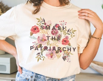 May include: A cream colored t-shirt with a floral design and the text "SMASH THE PATRIARCHY" printed in dark brown.