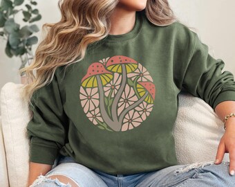 May include: A green sweatshirt with a circular graphic of stylized mushrooms and flowers in shades of pink, yellow, and green.