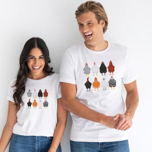 Puede incluir: Dos personas con camisetas blancas con un gr&aacute;fico colorido de pollos en la parte delantera. El gr&aacute;fico presenta nueve pollos en varios colores y patrones.