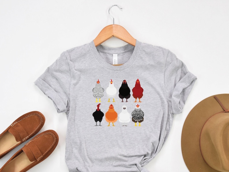Puede incluir: Una camiseta gris con un gr&aacute;fico de ocho pollos diferentes en varios colores y patrones. Los pollos est&aacute;n todos de espaldas al espectador.