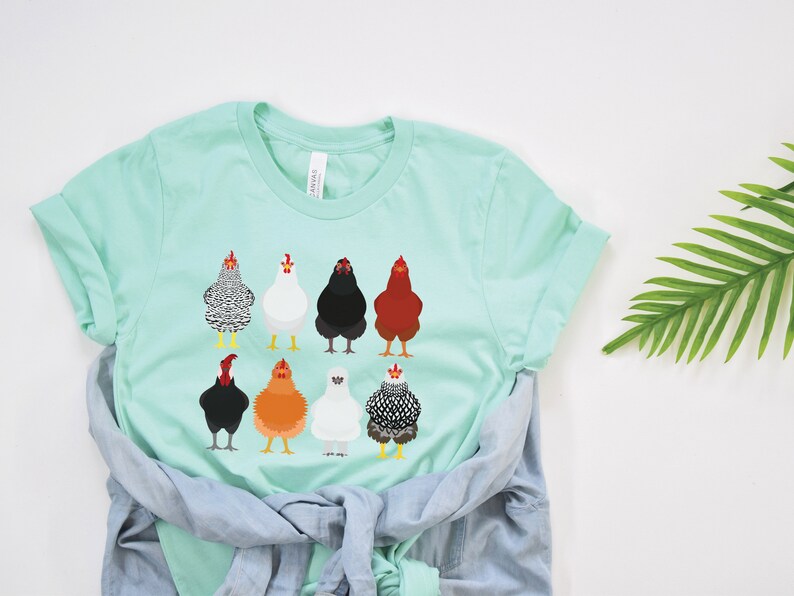 Puede incluir: Una camiseta azul claro con un gr&aacute;fico de ocho pollos diferentes en varios colores y patrones. Los pollos est&aacute;n todos mirando hacia adelante y tienen la cabeza levantada.
