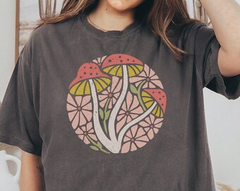 May include: A dark grey t-shirt with a graphic of pink and yellow mushrooms surrounded by pink flowers.