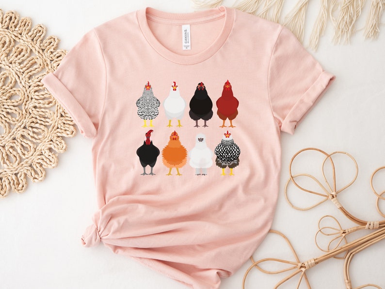 Puede incluir: Una camiseta rosa con un gr&aacute;fico de nueve pollos diferentes en varios colores y patrones. Los pollos est&aacute;n todos mirando hacia adelante y tienen las alas metidas.
