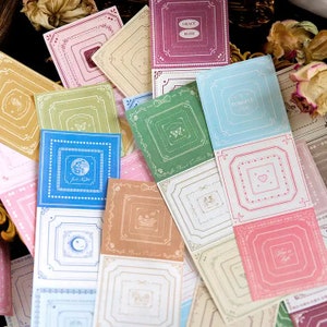 May include: A collection of colorful square stickers with ornate borders and various designs. The stickers feature pastel colors like pink, blue, and green, with text and illustrations such as butterflies, moons, and hearts. Some stickers have the text "Grace Bliss" and "I Forgive You".
