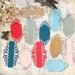 May include: Assortment of decorative paper die cuts in various colors and shapes. The die cuts feature intricate, ornate designs with a vintage aesthetic. The colors include red, teal, pink, brown, and blue.