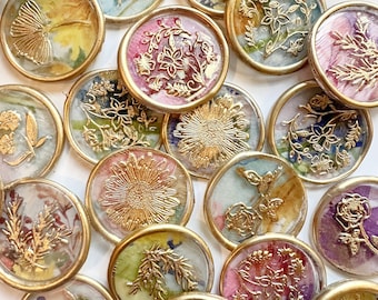 May include: A collection of 16 round wax seals with gold accents and floral designs. The seals are translucent and have a variety of colors, including pink, yellow, green, and blue.