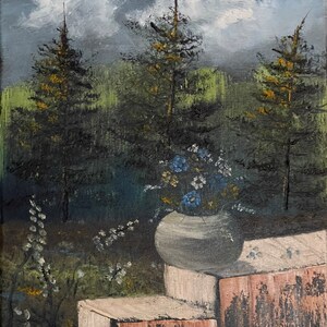 May include: An oil painting depicts a serene outdoor scene. Three tall pine trees stand against a backdrop of green foliage and a cloudy sky. A gray vase filled with blue and white flowers sits on a brick ledge.