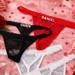 Peut inclure: Plusieurs strings en dentelle rouge, noire et blanche, avec des lettres en strass. Le string rouge porte l'inscription "DANIEL", le noir "CHRIS" et les blancs "BRIDE". Fond rose avec des c&oelig;urs.