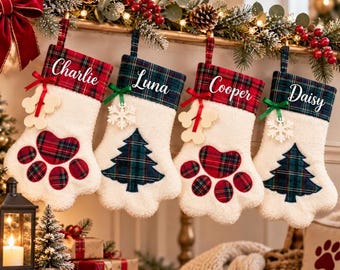 May include: Four Christmas stockings in white plush fabric with plaid cuffs. Two are paw-shaped with red plaid accents, and two are tree-shaped with green plaid accents. They feature the names Charlie, Luna, Cooper, and Daisy in white script.