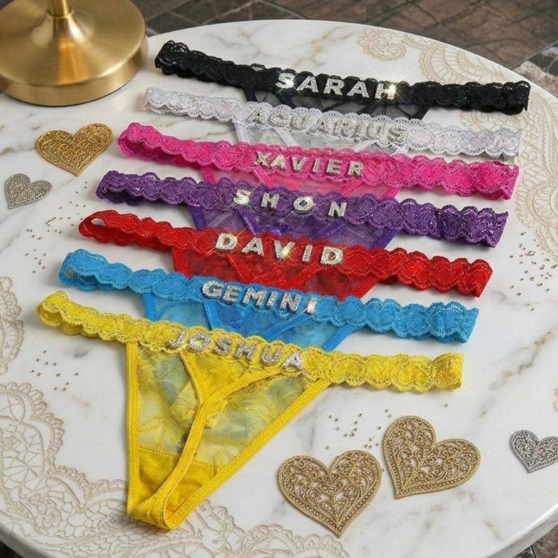 Peut inclure: Une collection de strings color&eacute;s avec des bordures en dentelle et des lettres en strass &eacute;pelant des noms et des signes du zodiaque. Les sous-v&ecirc;tements sont de diff&eacute;rentes couleurs, dont le noir, le blanc, le rose, le violet, le rouge, le bleu et le jaune. Des d&eacute;corations en forme de c&oelig;ur sont &eacute;parpill&eacute;es.