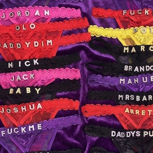 Peut inclure: Une collection de lingerie color&eacute;e, comprenant des strings et des bordures en dentelle assorties. La lingerie est de diff&eacute;rentes couleurs telles que le rose, le rouge, le noir, le violet et le jaune. Chaque pi&egrave;ce porte un nom ou un mot &eacute;pel&eacute; en lettres scintillantes.