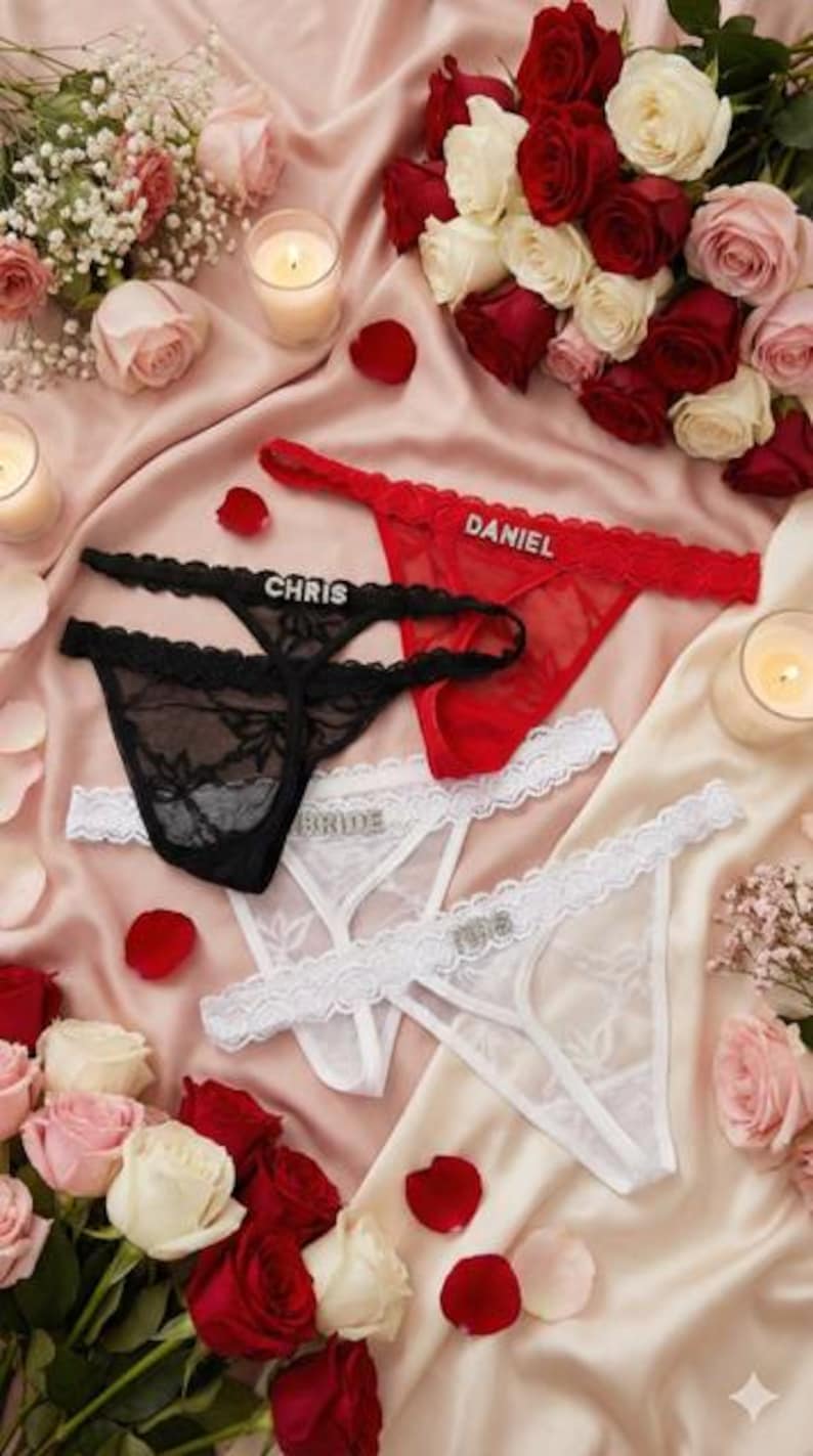 Peut inclure: Ensemble de strings rouges, noirs et blancs, avec bordures en dentelle et ornements en strass. Les noms "CHRIS", "DANIEL" et "BRIDE" sont affich&eacute;s. Dispos&eacute;s sur une surface satin&eacute;e rose avec des roses et des bougies.