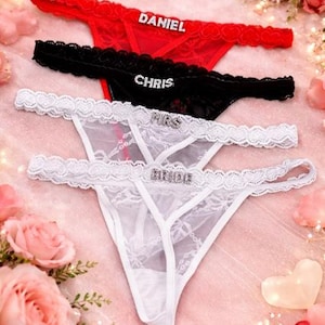 Peut inclure: Ensemble de strings rouges, noirs et blancs, orn&eacute;s de lettres en strass. Le string rouge porte l'inscription "DANIEL", le noir "CHRIS", et les blancs "MRS" et "BRIDE". La lingerie est pr&eacute;sent&eacute;e sur un fond rose avec des roses.