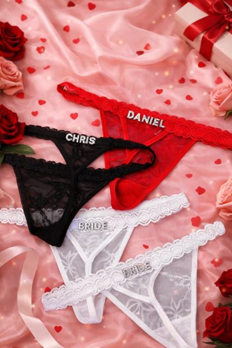 Peut inclure: Plusieurs strings en dentelle rouge, noire et blanche, avec des lettres en strass. Le string rouge porte l'inscription "DANIEL", le noir "CHRIS" et les blancs "BRIDE". Fond rose avec des c&oelig;urs.